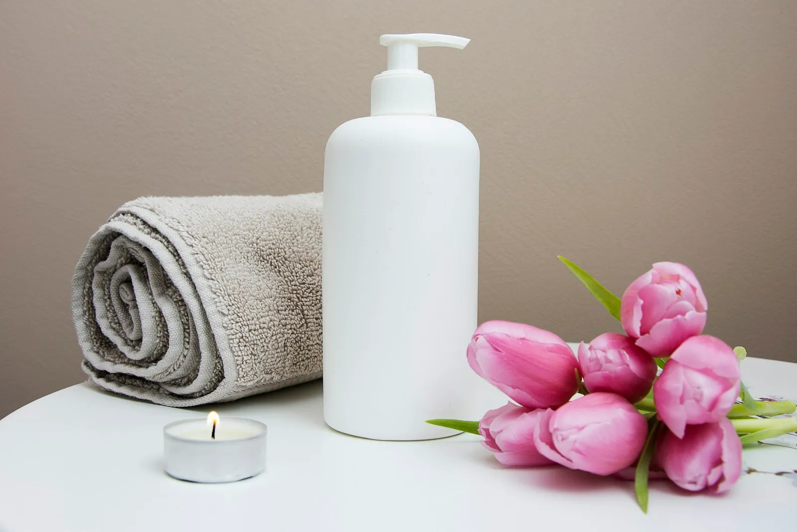 A calm wellness treatment space with a towel, candle and fresh flowers