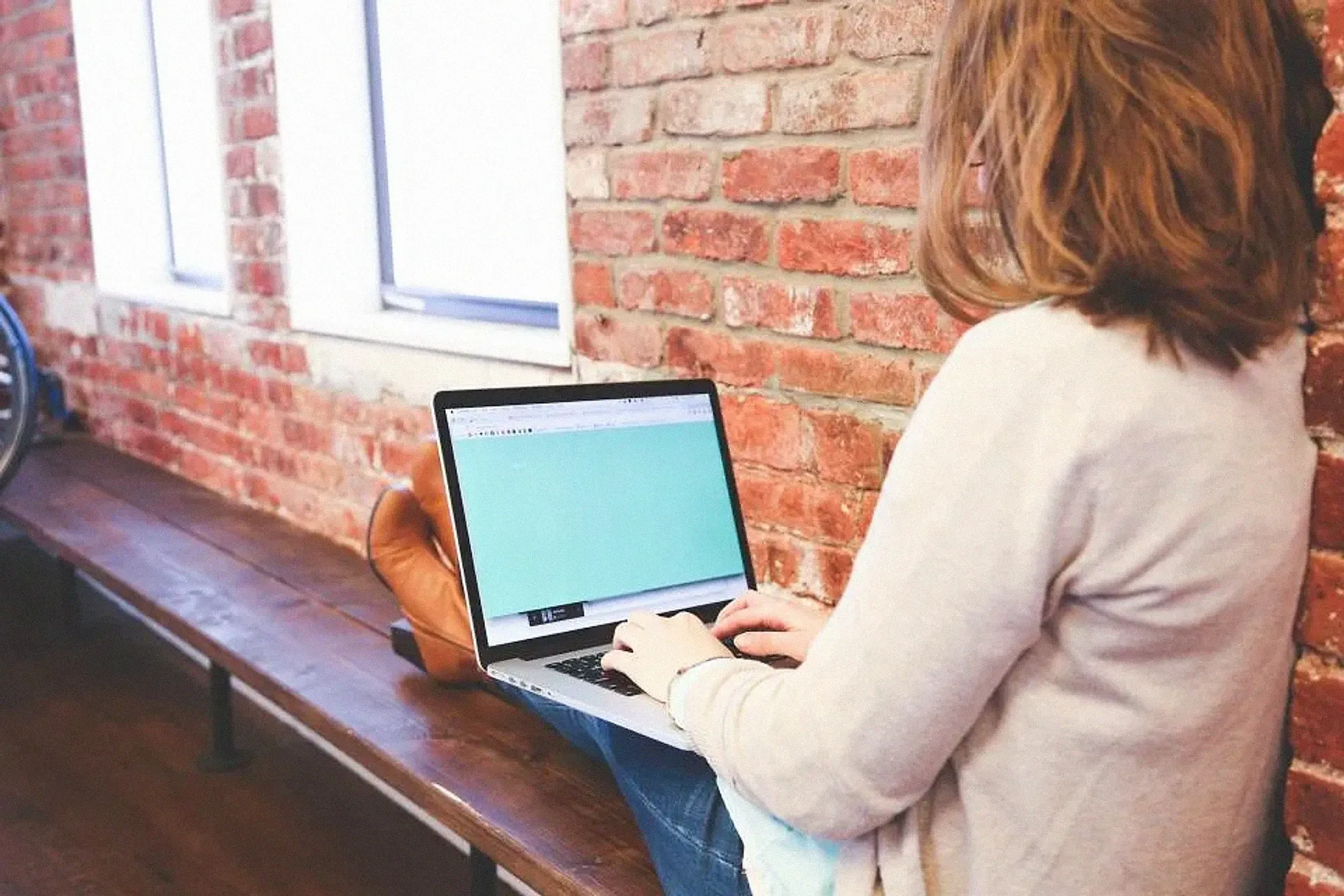 A woman typing on a laptop beside a brick wall