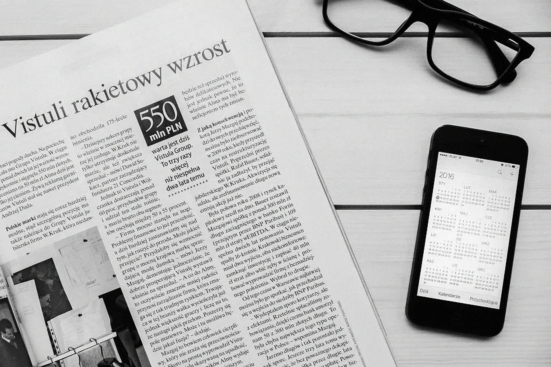 A newspaper and a smartphone on a desk with reading glasses