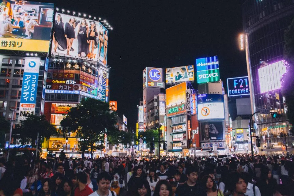A busy city crossing lit by bright advertising signs at night